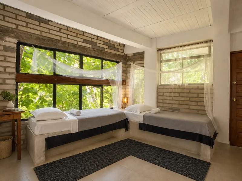 Sala con dos camas preparadas junto a ventanales con vegetación
