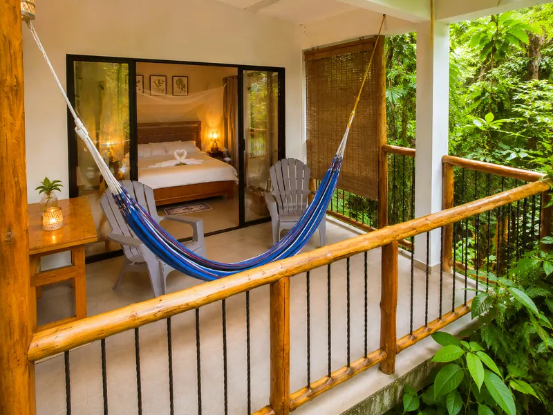 Terraza con hamaca azul y sillas de madera; al fondo, la habitación principal tras puertas de vidrio